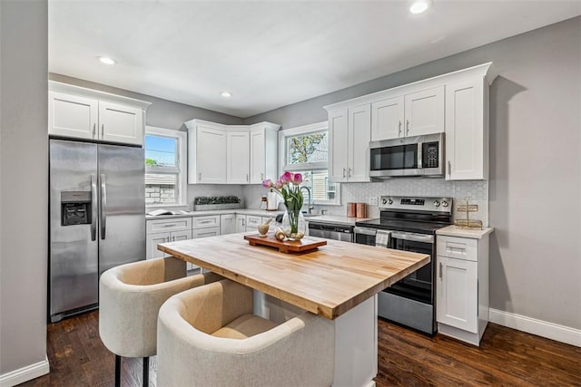 kitchen with butcher block countertops, white cabinetry, a wealth of natural light, and stainless steel appliances