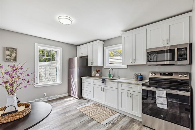 kitchen featuring white cabinets, appliances with stainless steel finishes, a sink, light countertops, and light wood-style flooring