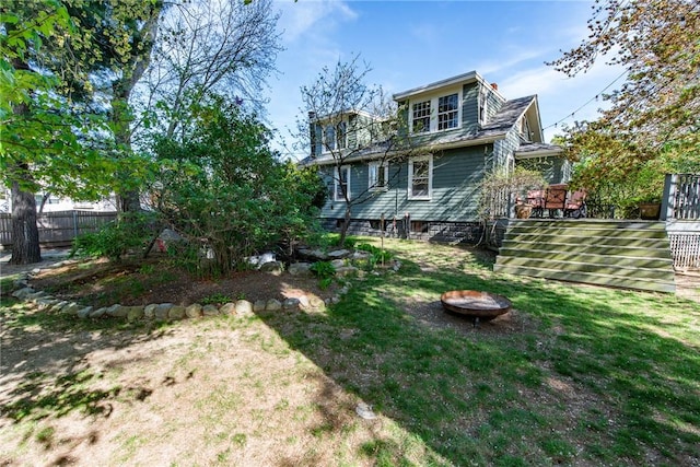 back of house with a lawn, an outdoor fire pit, fence, and a deck