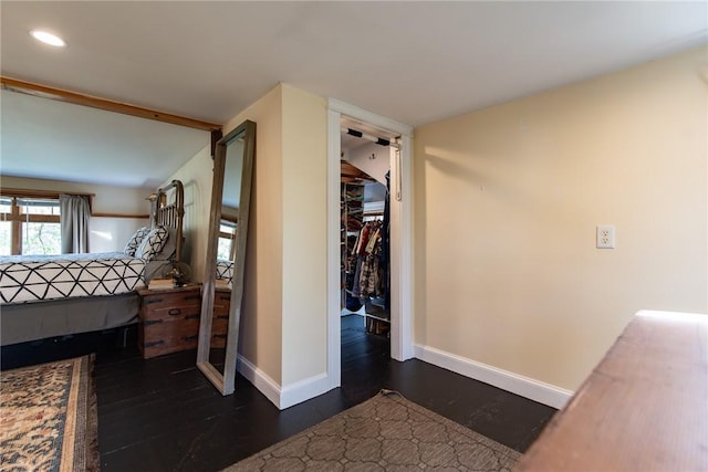 unfurnished bedroom featuring dark wood-style flooring, baseboards, recessed lighting, and a walk in closet