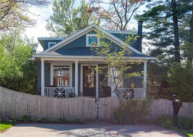 view of front of property featuring roof with shingles, a fenced front yard, and a porch