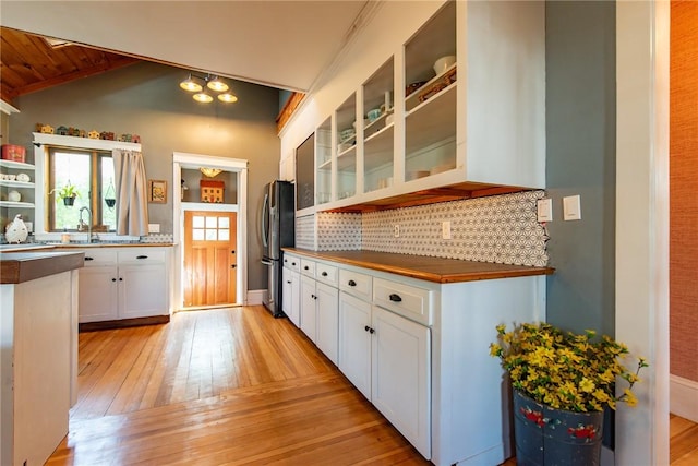 kitchen with tasteful backsplash, vaulted ceiling, white cabinets, glass insert cabinets, and light wood-style flooring