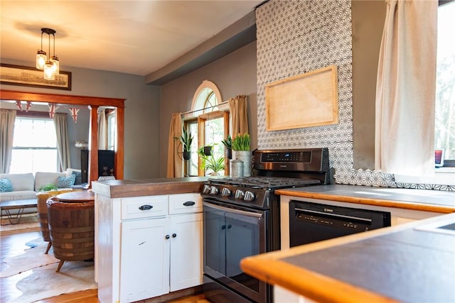 kitchen with a peninsula, wood finished floors, stainless steel range with gas cooktop, white cabinets, and decorative light fixtures