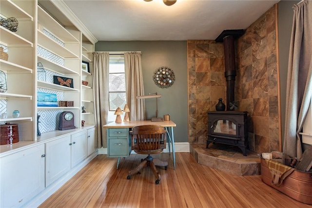 office space featuring baseboards, a wood stove, and light wood-style floors