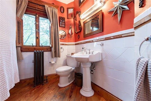 bathroom with toilet, radiator heating unit, a wainscoted wall, tile walls, and hardwood / wood-style flooring