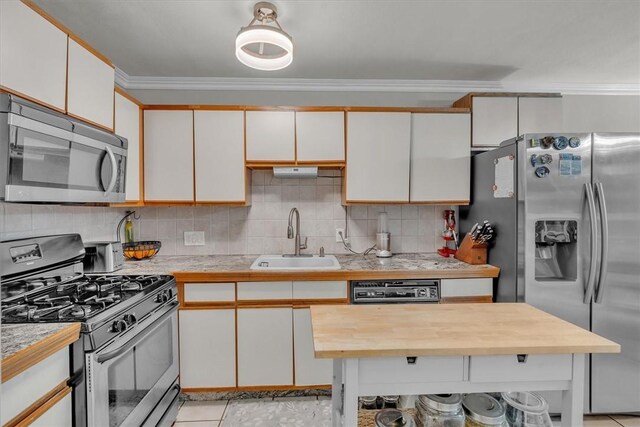 kitchen featuring crown molding, a sink, butcher block countertops, stainless steel appliances, and decorative backsplash