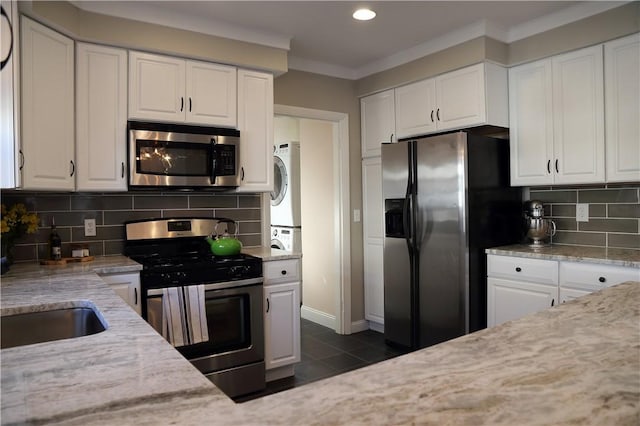 kitchen featuring white cabinets, stacked washer / drying machine, stainless steel appliances, recessed lighting, and decorative backsplash
