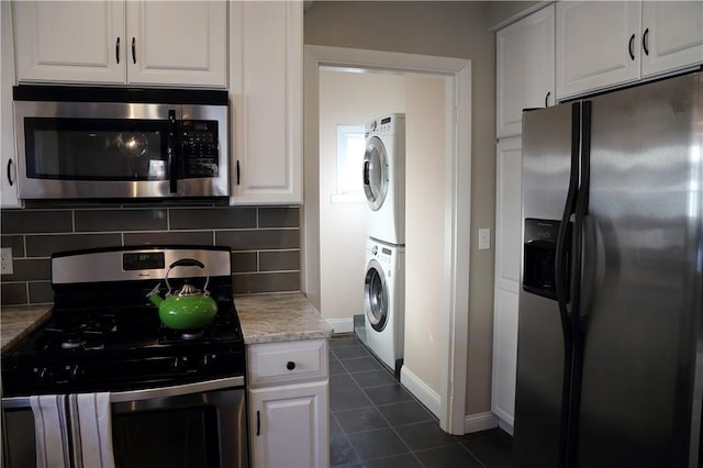 kitchen with stacked washing maching and dryer, white cabinets, dark tile patterned flooring, tasteful backsplash, and appliances with stainless steel finishes