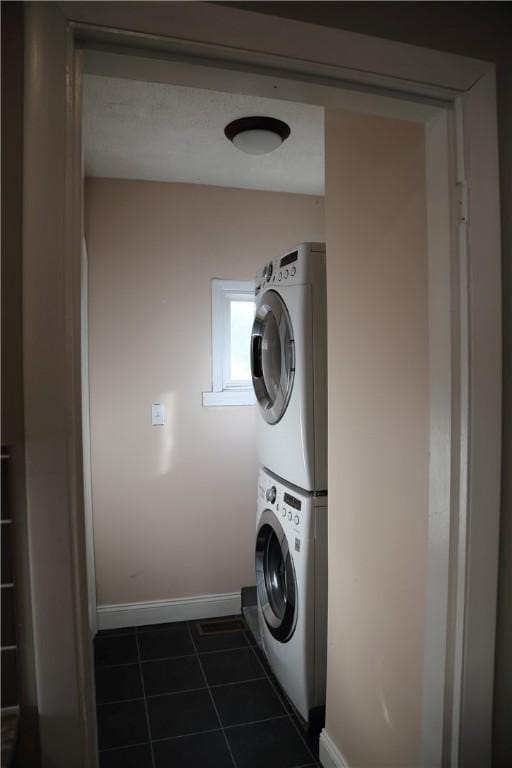 laundry room featuring baseboards, stacked washer and clothes dryer, dark tile patterned floors, and laundry area
