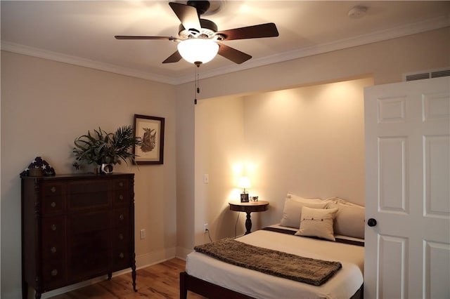 bedroom with crown molding, ceiling fan, baseboards, wood finished floors, and visible vents
