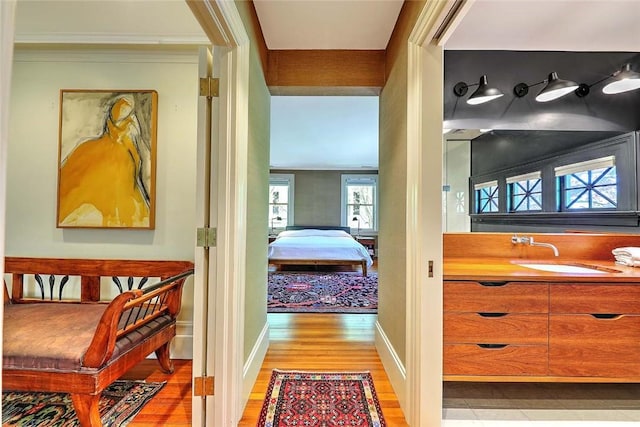 hallway featuring light wood-style floors, a sink, baseboards, and crown molding