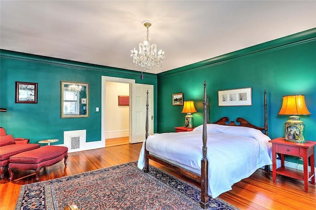 bedroom with crown molding, visible vents, wood finished floors, baseboards, and a notable chandelier