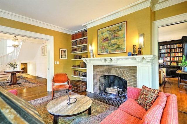 living room featuring built in shelves, ornamental molding, a fireplace, and wood finished floors