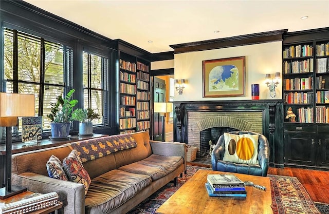 living area featuring ornamental molding, built in features, a brick fireplace, and wood finished floors