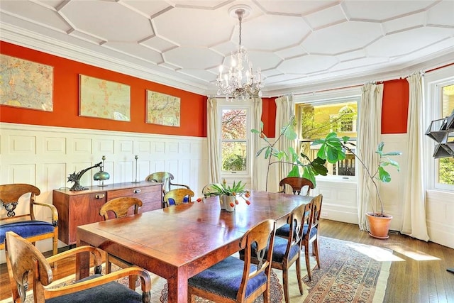 dining space with an inviting chandelier, light wood-style flooring, crown molding, and a decorative wall