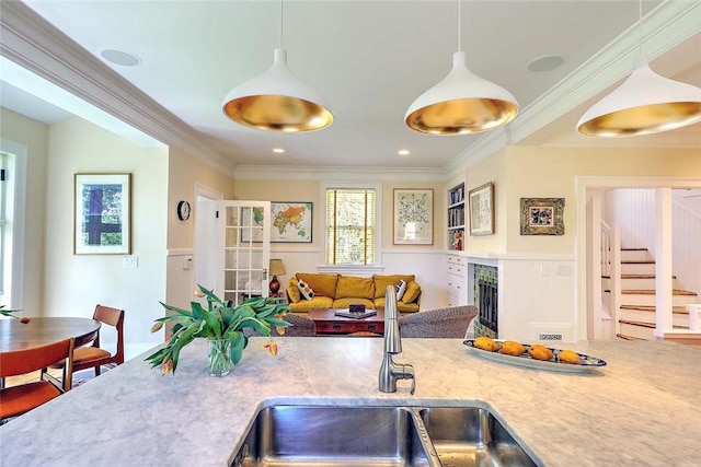 kitchen with hanging light fixtures, a sink, light countertops, open floor plan, and ornamental molding