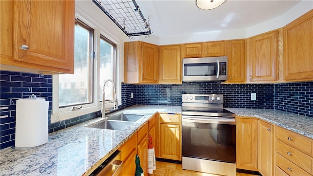 kitchen with light stone counters, a sink, appliances with stainless steel finishes, and backsplash