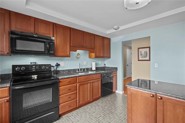 kitchen with brown cabinetry, a tray ceiling, a sink, dark stone countertops, and black appliances