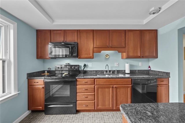 kitchen featuring brown cabinets, a sink, light tile patterned floors, black appliances, and dark stone counters