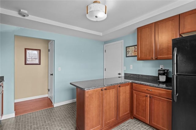 kitchen with freestanding refrigerator, a peninsula, light tile patterned flooring, and brown cabinets