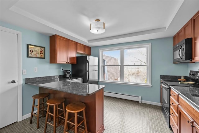 kitchen featuring a breakfast bar, baseboard heating, baseboards, a tray ceiling, and black appliances