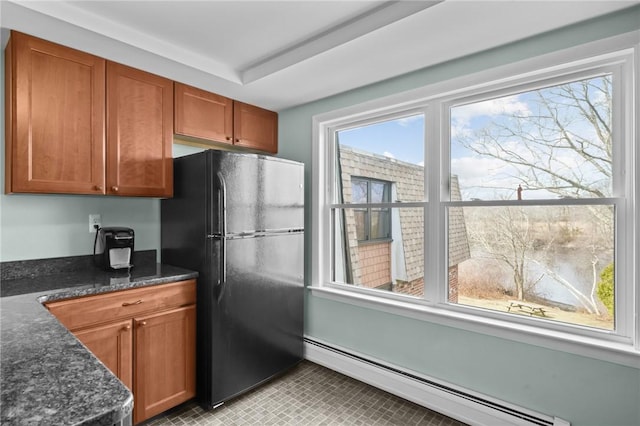 kitchen featuring brown cabinets, built in desk, baseboard heating, freestanding refrigerator, and dark stone counters