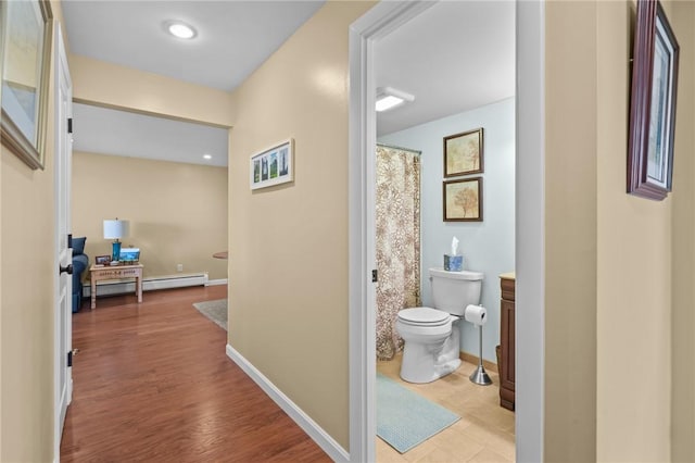 hall with baseboards, a baseboard heating unit, and wood finished floors