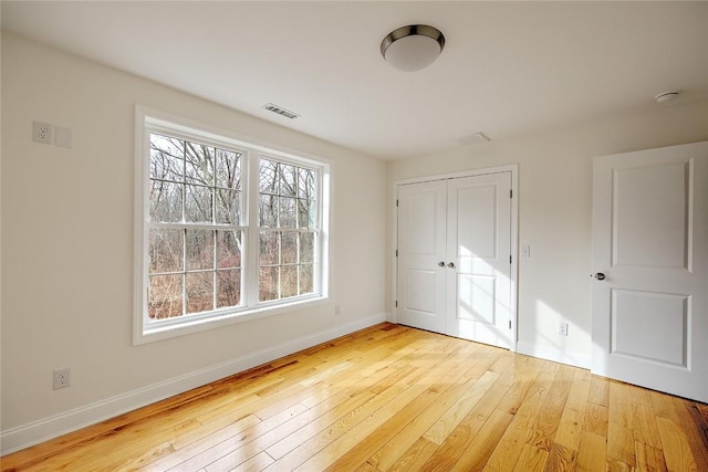 unfurnished bedroom with baseboards, a closet, light wood-type flooring, and visible vents