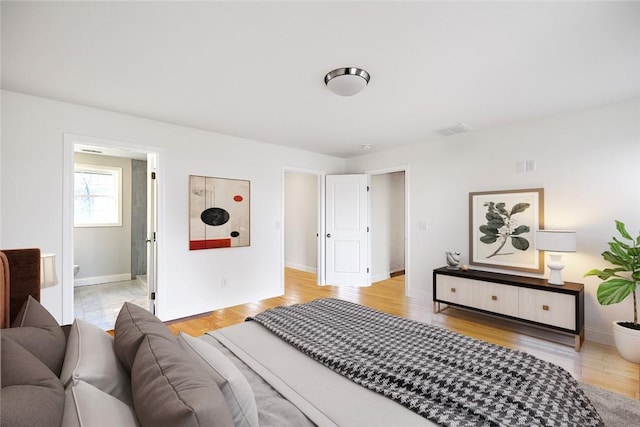 bedroom featuring visible vents, light wood-style floors, ensuite bath, and baseboards