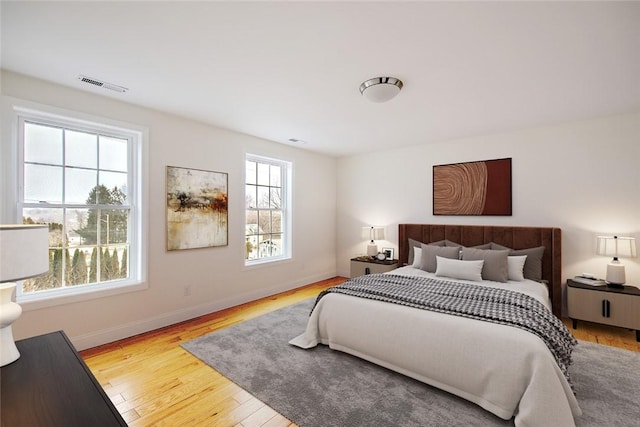 bedroom featuring baseboards, visible vents, multiple windows, and wood finished floors