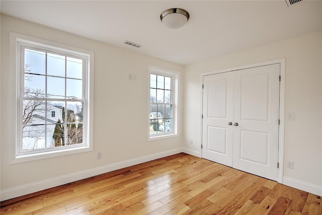 unfurnished bedroom with baseboards, a closet, light wood-type flooring, and visible vents