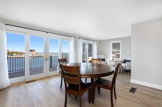 dining area featuring baseboards, light wood finished floors, visible vents, and a water view