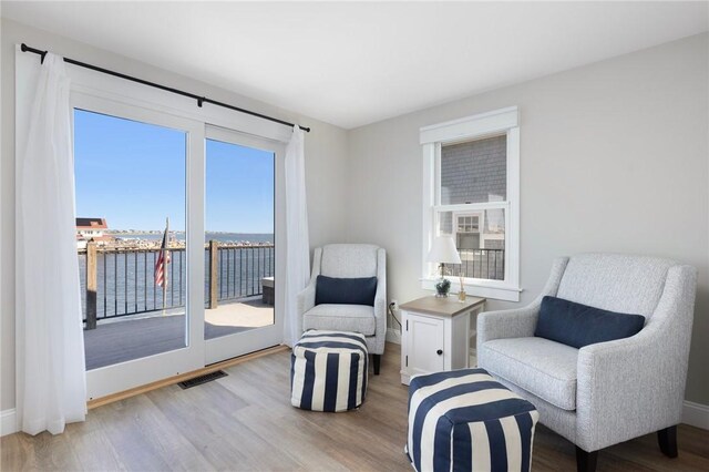 sitting room featuring a water view, visible vents, wood finished floors, and baseboards