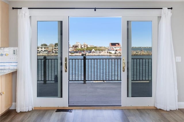 doorway to outside with a water view, wood finished floors, plenty of natural light, visible vents, and baseboards
