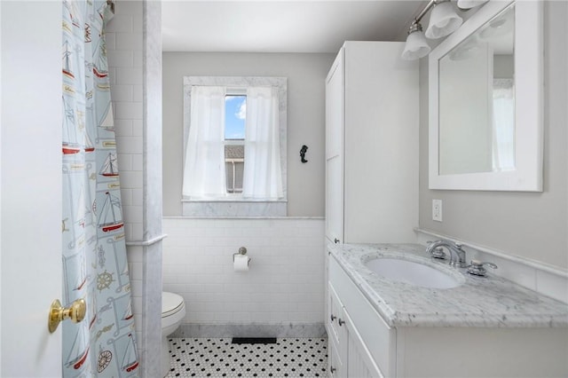 full bath with tile walls, toilet, tile patterned floors, vanity, and a wainscoted wall