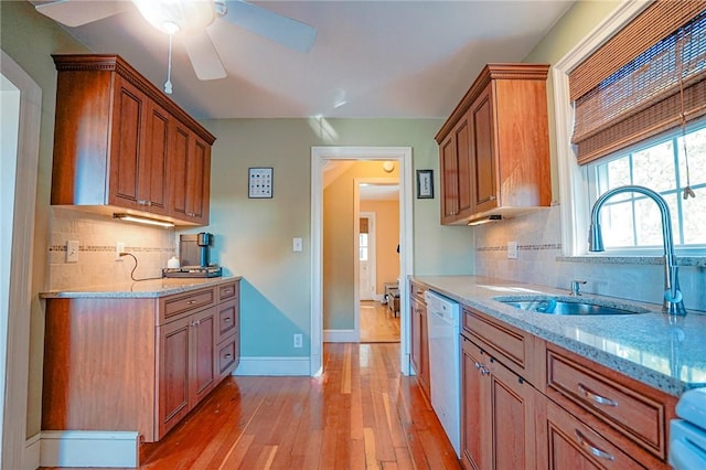 kitchen featuring a ceiling fan, light stone counters, a sink, light wood-style flooring, and backsplash