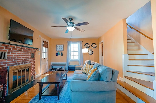 living area featuring stairs, wood finished floors, a fireplace, baseboards, and a ceiling fan