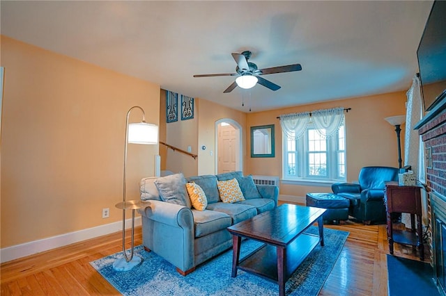living room featuring baseboards, arched walkways, a brick fireplace, and wood finished floors