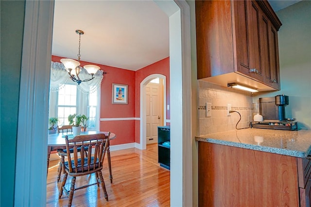kitchen with arched walkways, tasteful backsplash, light stone counters, a chandelier, and light wood-style flooring