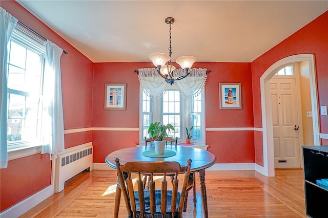 dining space with light wood-style floors, baseboards, radiator heating unit, and a notable chandelier