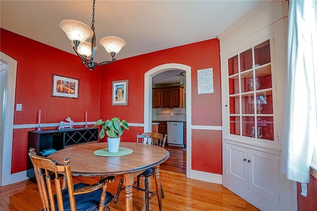 dining area with light wood-type flooring, arched walkways, baseboards, and an inviting chandelier