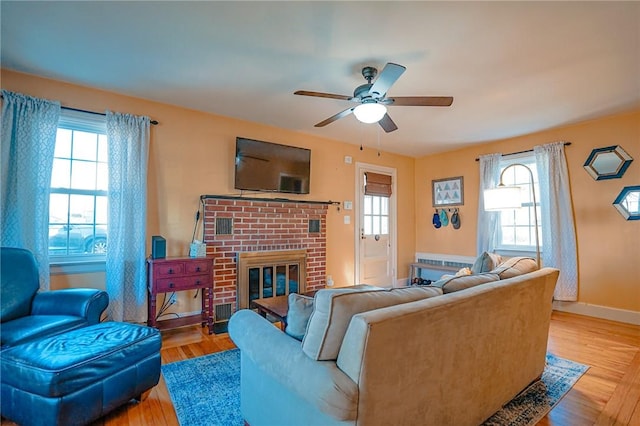 living area featuring a brick fireplace, a ceiling fan, baseboards, and wood finished floors