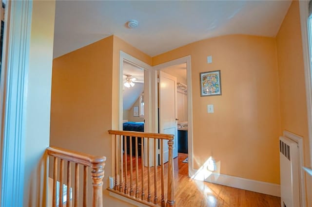 hall featuring radiator heating unit, baseboards, an upstairs landing, wood finished floors, and lofted ceiling
