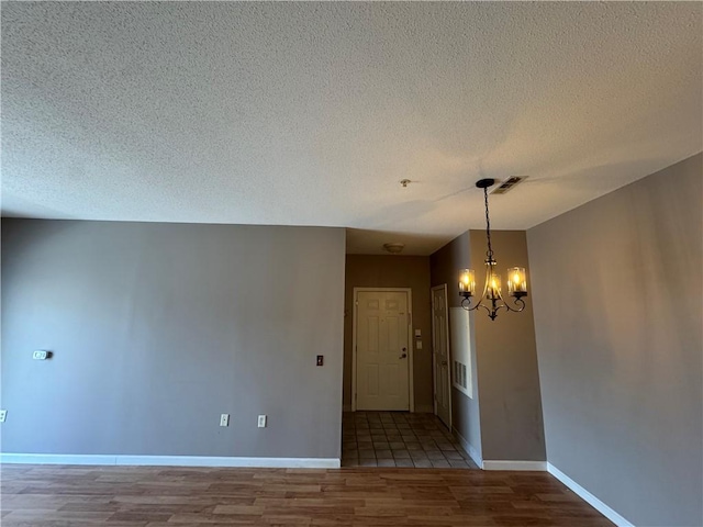 spare room with visible vents, wood finished floors, baseboards, a textured ceiling, and a notable chandelier