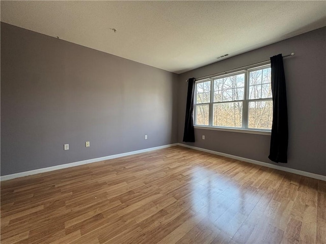 empty room featuring light wood-style floors, a textured ceiling, baseboards, and visible vents