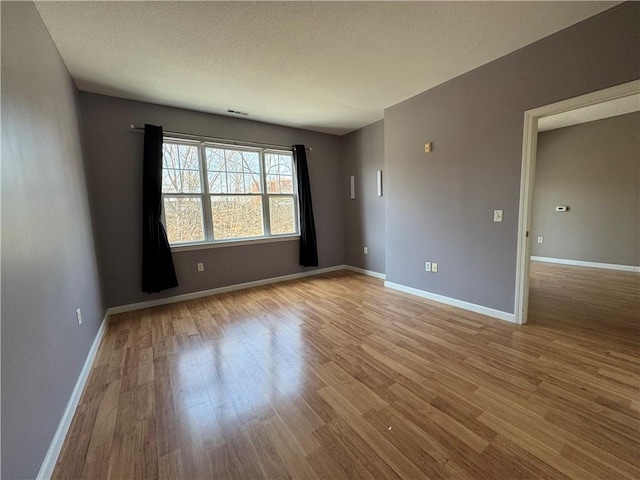 empty room featuring a textured ceiling, baseboards, and light wood finished floors