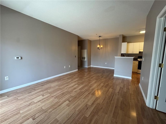 unfurnished living room with baseboards, a textured ceiling, wood finished floors, and a notable chandelier