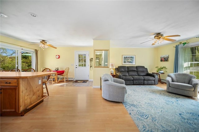 living room with baseboards, baseboard heating, a ceiling fan, and light wood-style flooring