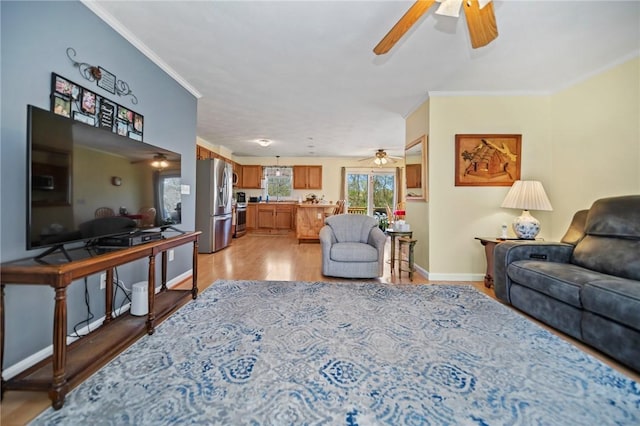 living area featuring baseboards, a ceiling fan, light wood-style flooring, and ornamental molding