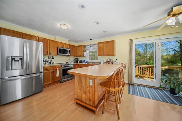 kitchen featuring brown cabinetry, a peninsula, a kitchen bar, light countertops, and stainless steel appliances